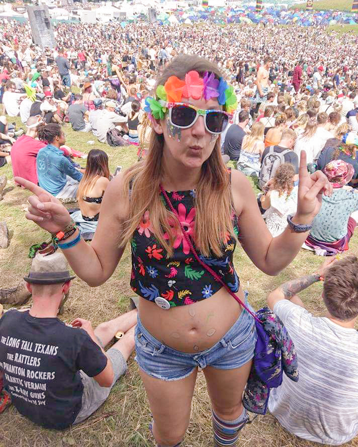 21 weeks pregnant lady in colourful clothing at a music festival giving peace signs